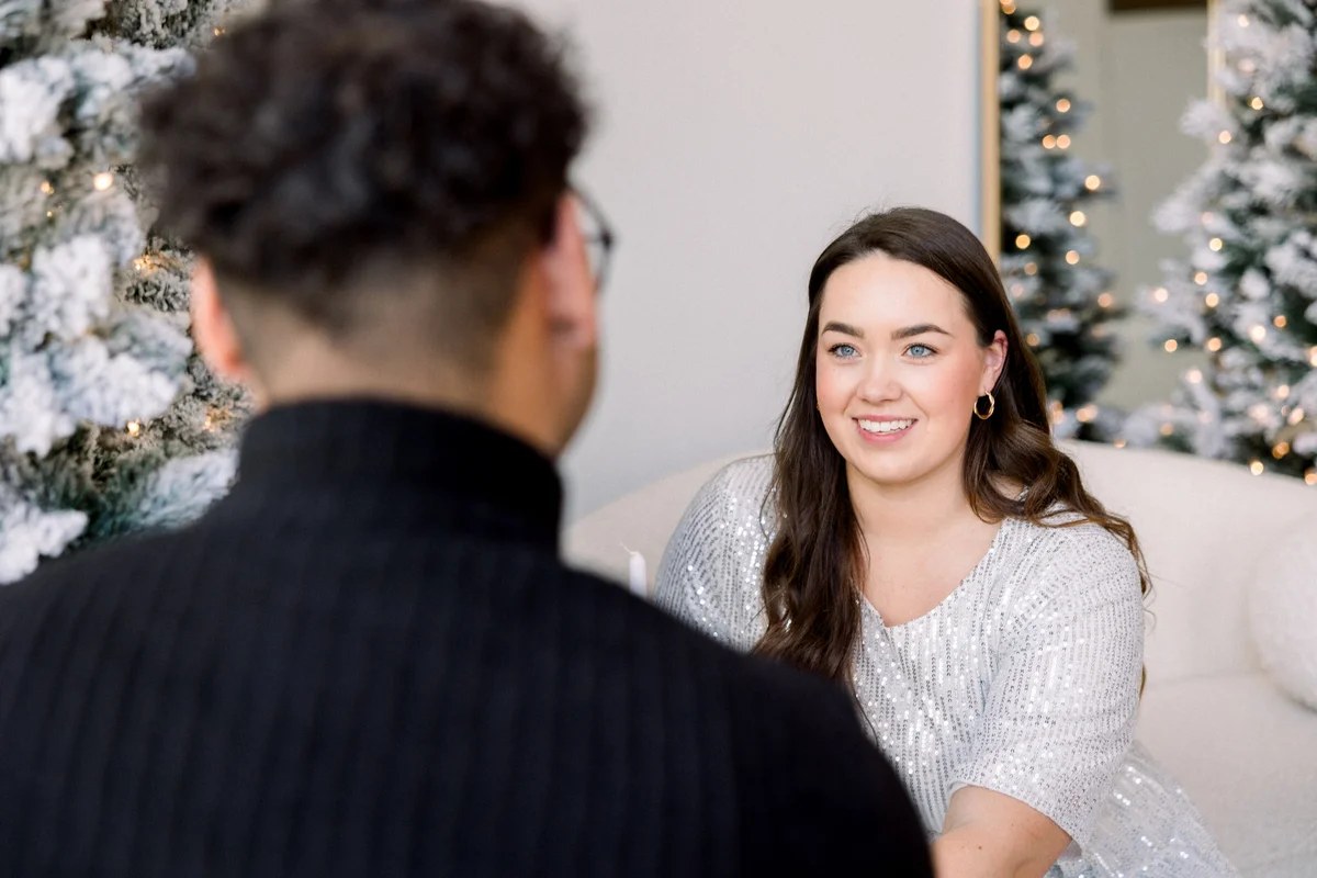 Couple sharing a candid moment by snowy holiday trees during an indoor studio session in Chicago