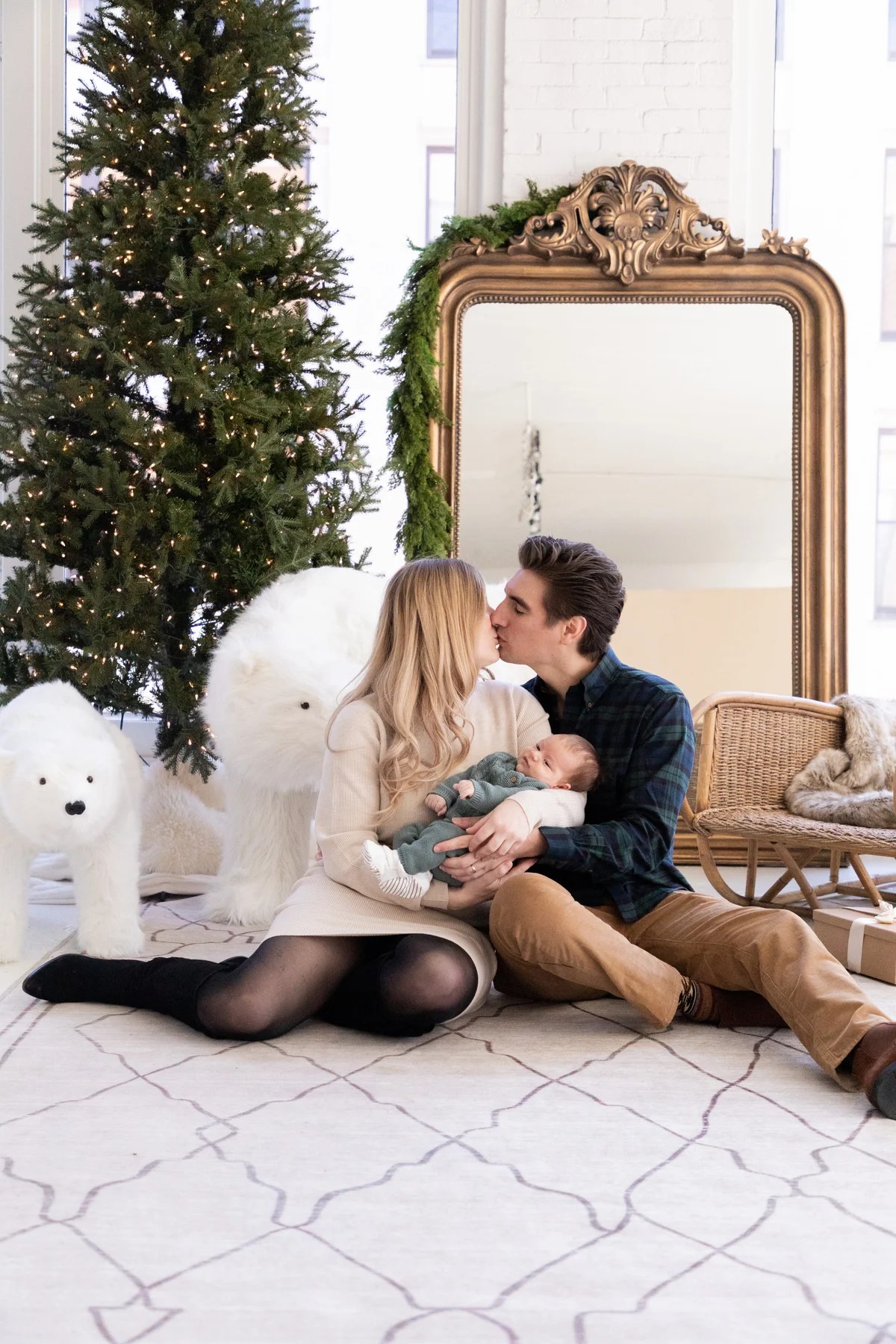 Parents kissing while holding their newborn beside a Christmas tree during a Chicago holiday mini session