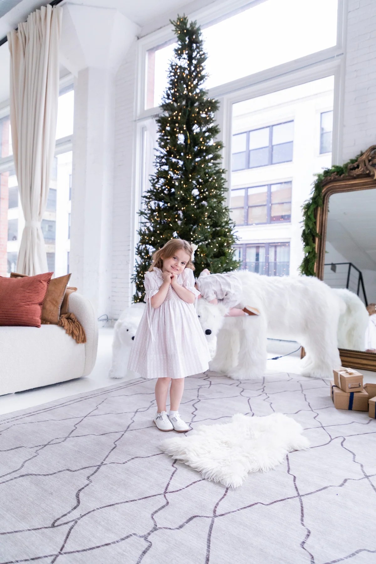 Toddler girl in a smocked pastel dress by a Christmas tree, a classic holiday photo outfit idea